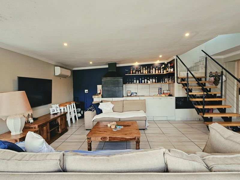 Open-plan living area featuring a built-in fireplace, tiled flooring, and a modern staircase, with visible ceiling water staining requiring attention.