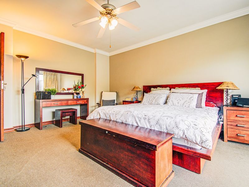 A spacious bedroom featuring neutral wall tones, crown molding, a ceiling fan, and carpeted flooring.