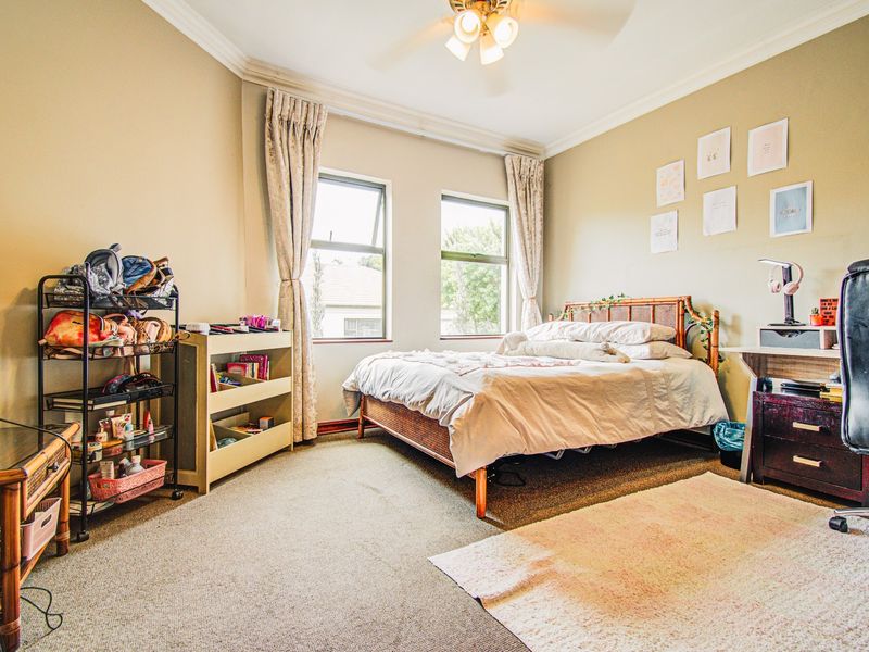A well-lit bedroom featuring neutral wall tones, carpeted flooring, crown molding, and a ceiling fan, providing a comfortable and functional living space.