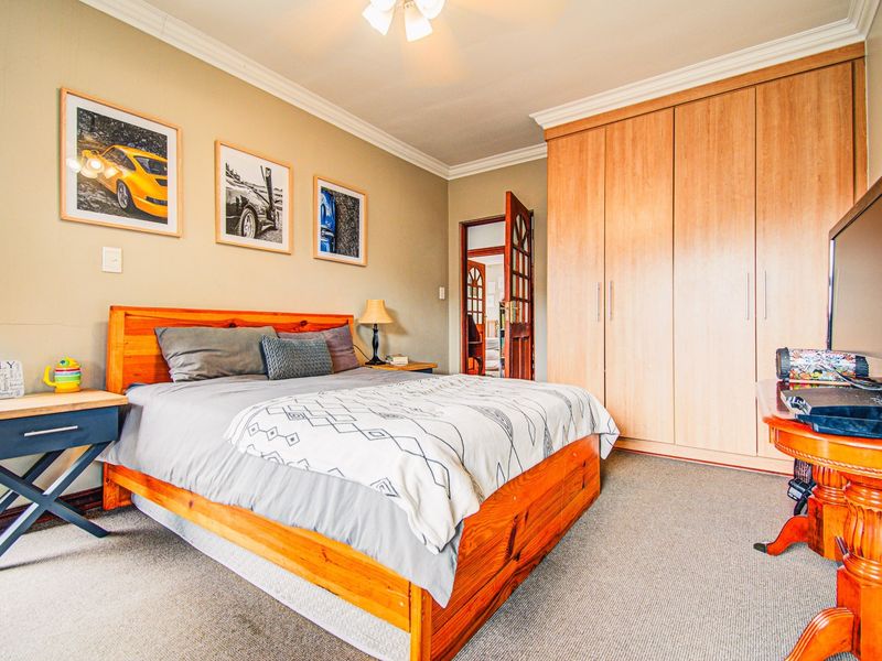 A well-maintained bedroom featuring neutral walls, carpeted flooring, crown molding, and extensive built-in wooden cupboards for storage.