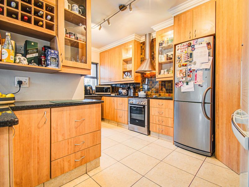 A functional kitchen featuring light wood cabinetry, granite countertops, stainless steel appliances, a tiled backsplash, and integrated wine storage.