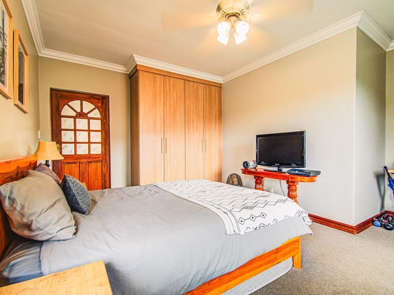 A comfortable bedroom featuring built-in wooden wardrobes, crown molding, and a ceiling fan, providing a functional and well-maintained living space.