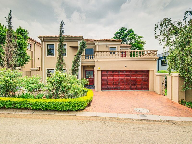 A well-maintained double-story residence featuring a brick-paved driveway, a double garage, and an upper-level balcony with decorative balustrades.