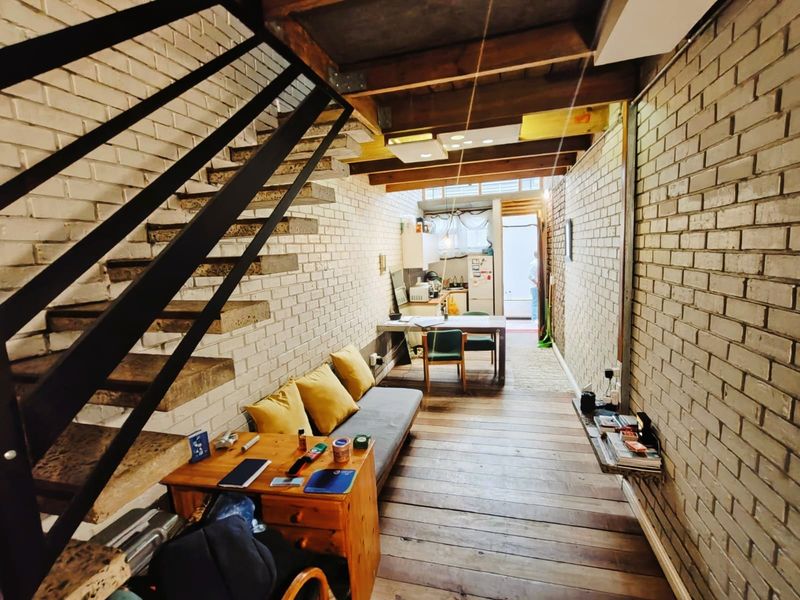 Open-plan commercial space featuring exposed brick walls, timber flooring, and a prominent staircase, leading to a functional kitchen area at the rear.
