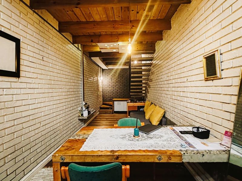An open-plan commercial space featuring exposed brick walls, timber ceiling beams, and a wooden staircase, offering a rustic and industrial aesthetic.