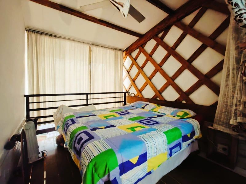 Bedroom featuring exposed timber ceiling beams, decorative lattice wall paneling, and timber flooring, with a metal balustrade overlooking the lower level.