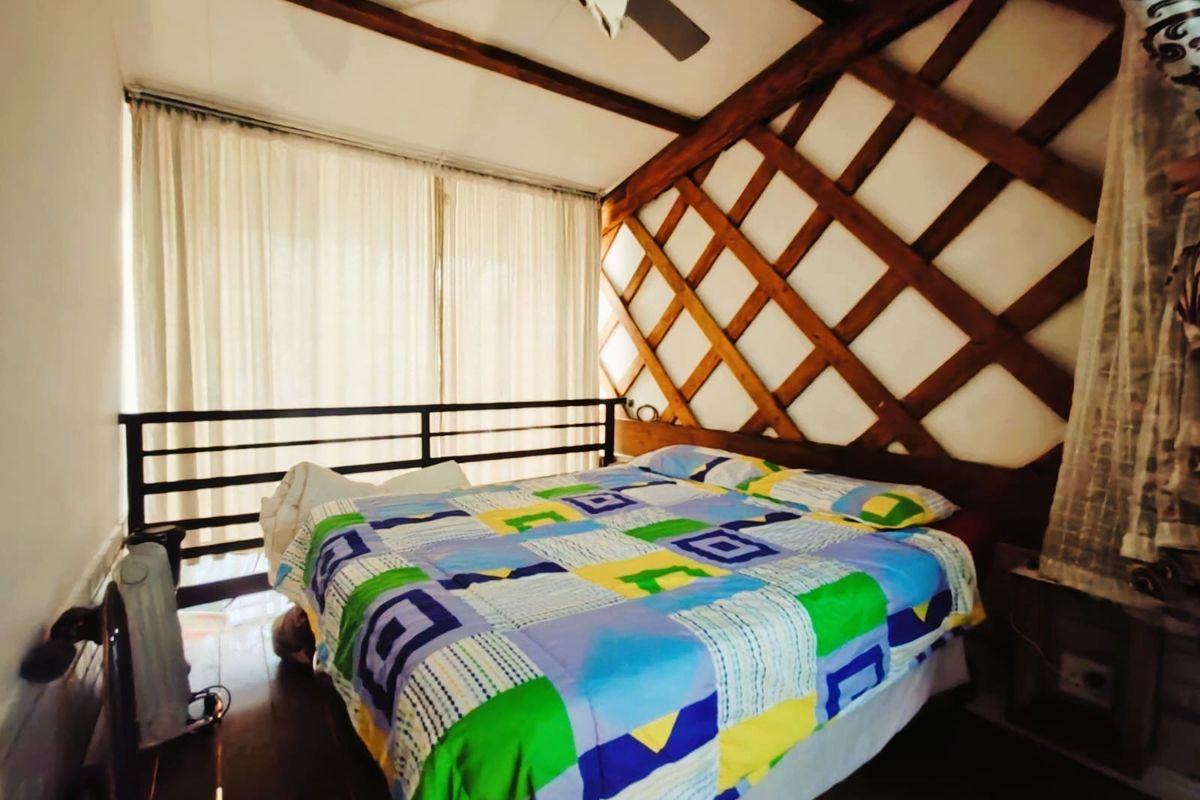 Bedroom featuring exposed timber ceiling beams, decorative lattice wall paneling, and timber flooring, with a metal balustrade overlooking the lower level.