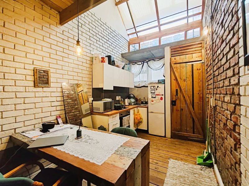 An open-plan kitchen and dining area featuring exposed brick walls, timber flooring, and a large skylight providing natural light.