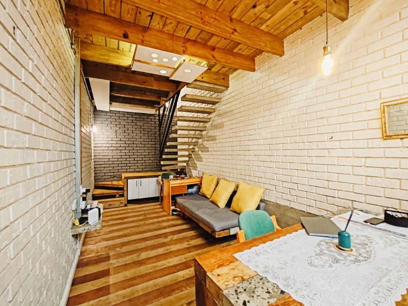 Open-plan commercial space featuring exposed timber ceiling beams, painted brick walls, and an open staircase with integrated cabinetry.