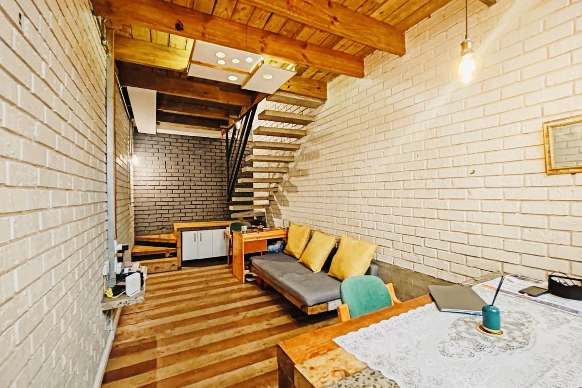 Open-plan commercial space featuring exposed timber ceiling beams, painted brick walls, and an open staircase with integrated cabinetry.