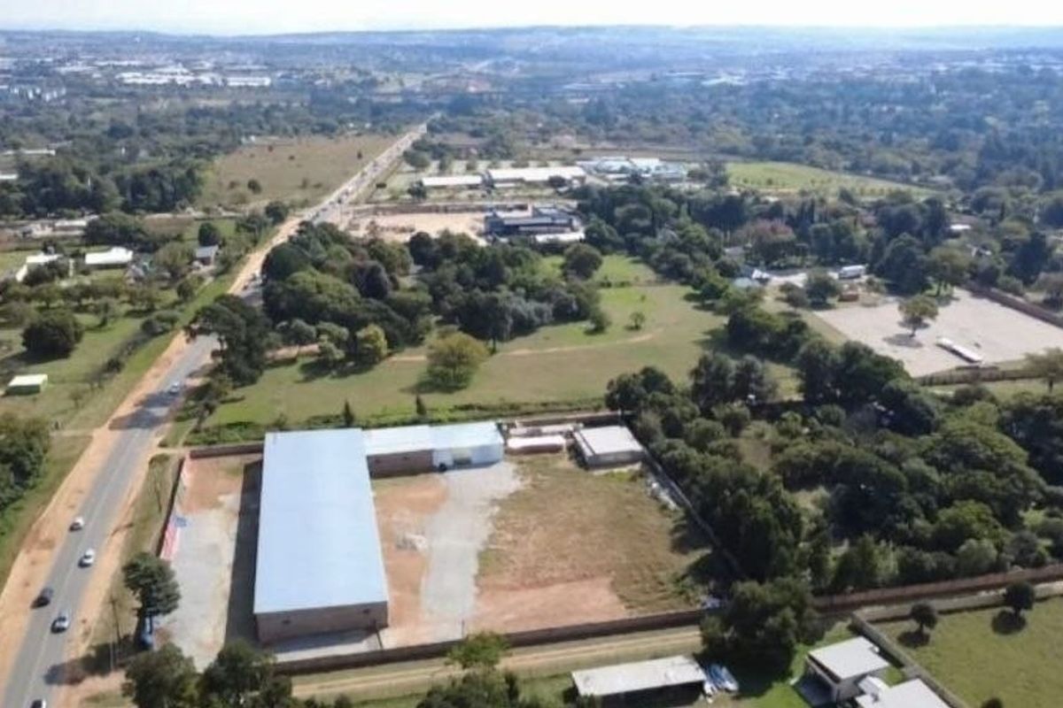 Aerial view of a commercial property featuring a large warehouse structure with a metal roof, situated on a spacious plot with perimeter fencing.
