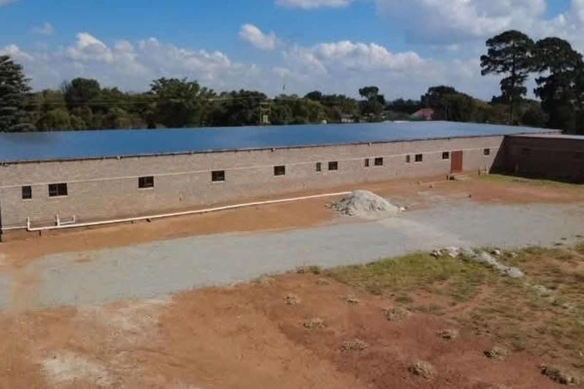 Aerial view of a large commercial warehouse building featuring a metal roof and brick exterior, situated on a spacious, undeveloped plot of land.