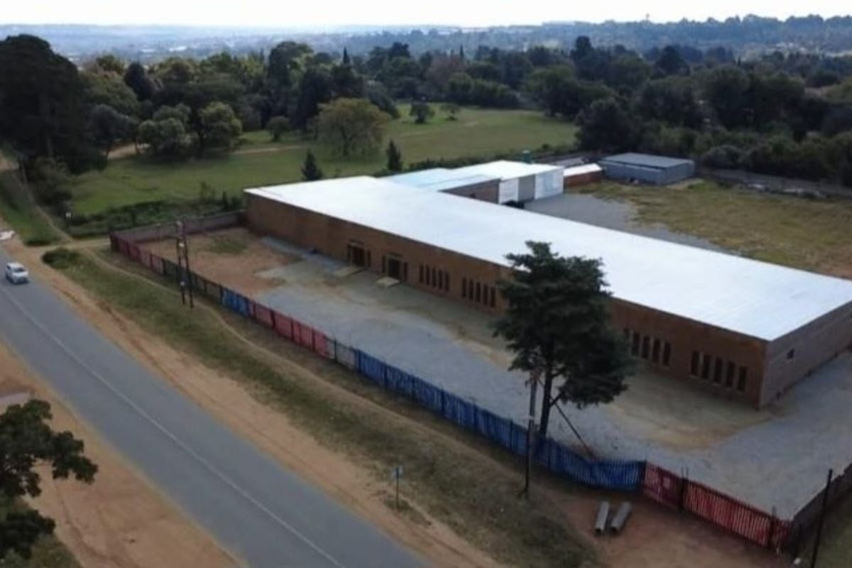 Aerial view of a commercial property featuring a large warehouse-style building with a metal roof, perimeter fencing, and surrounding open yard space.