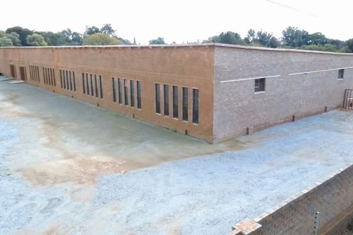 An elevated view of a commercial building featuring a brick facade, large windows, and a secure perimeter wall with electric fencing and a gravel yard.