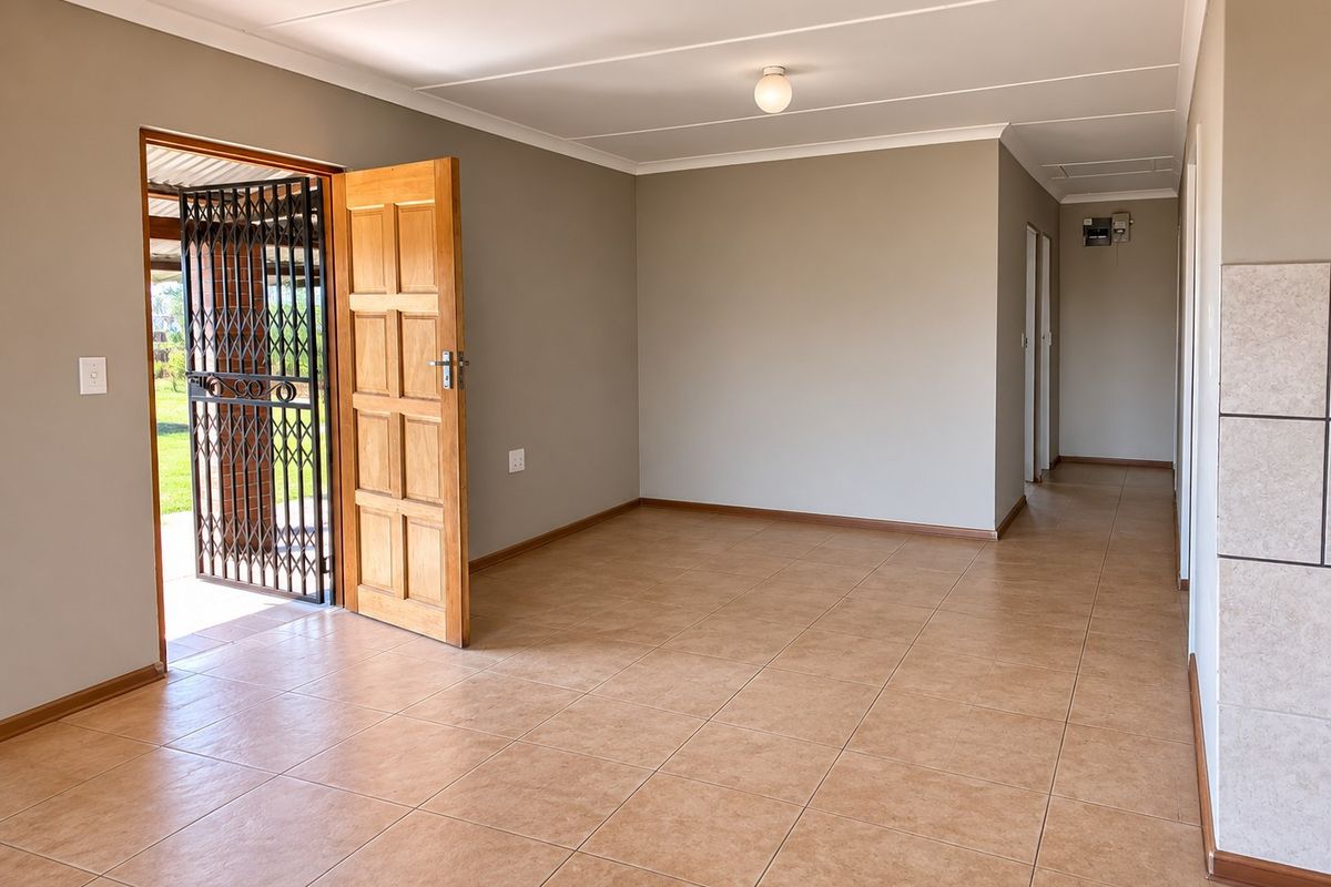 A bright, empty living area featuring neutral wall tones, tiled flooring, and direct access to the exterior through a timber door with a security gate.