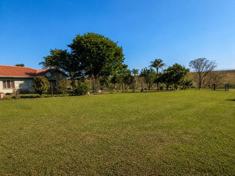 A spacious, well-maintained garden featuring a large lawn, mature trees, and perimeter fencing, adjacent to the side elevation of the house.