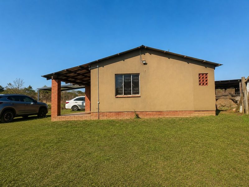Rear view of a single-story house featuring a covered patio area, brick foundation plinth, and security-fitted windows set within a large grassed yard.