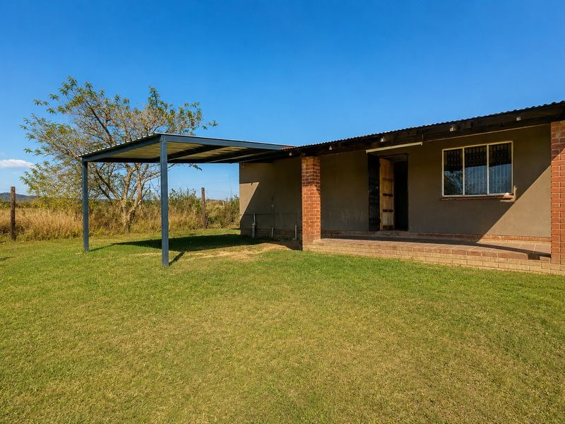 Rear view of the property featuring a covered patio area, attached carport, and brick structural elements set within a spacious garden.