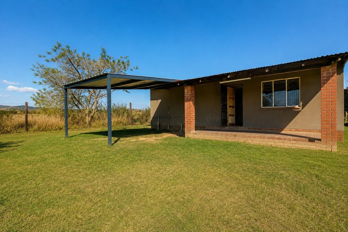 Rear view of the property featuring a covered patio area, attached carport, and brick structural elements set within a spacious garden.