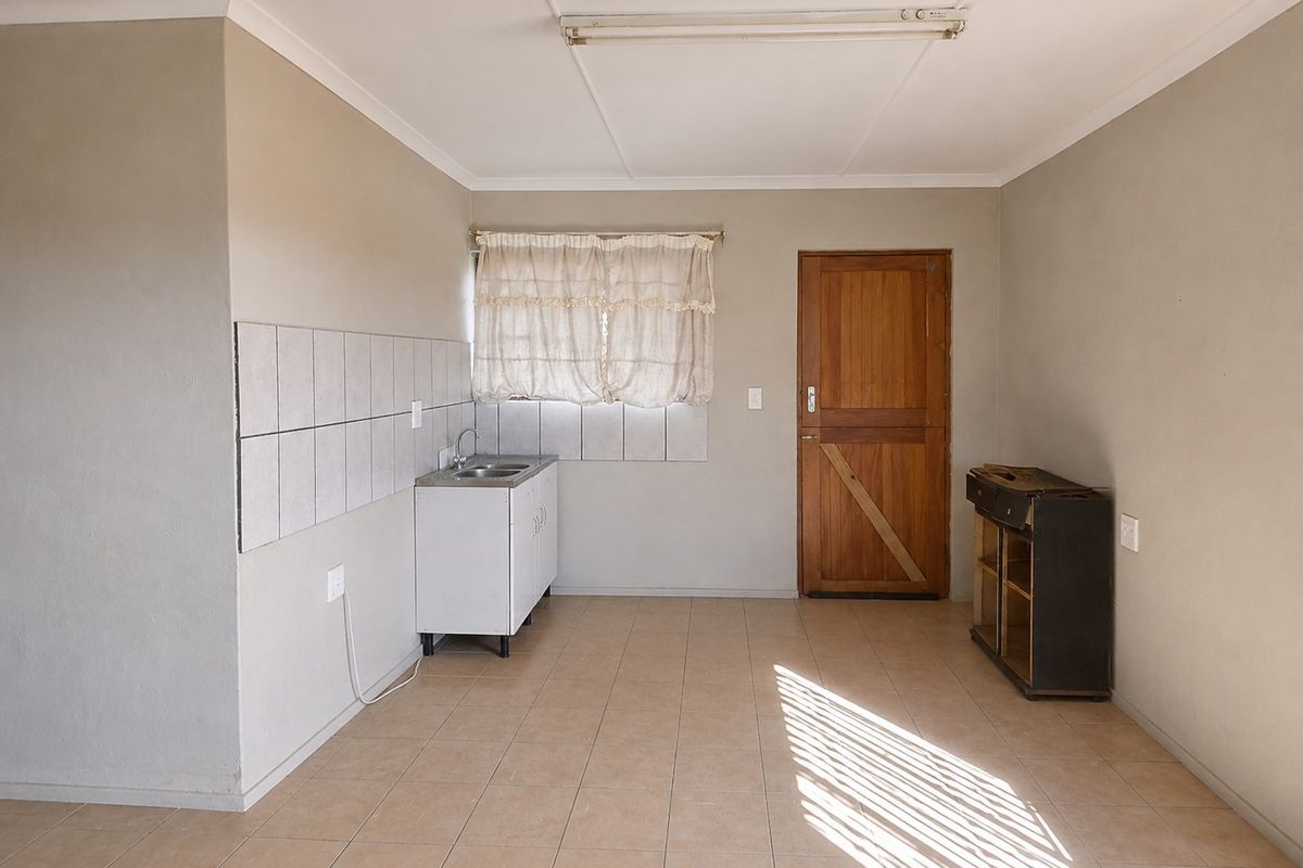 A basic, empty kitchen area featuring tiled flooring, a small sink unit with splashback, and a wooden exterior door.