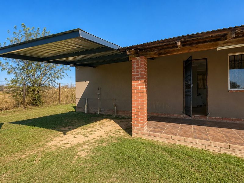 A covered patio area featuring a metal carport extension, brick support pillar, and tiled flooring, providing a functional outdoor space.