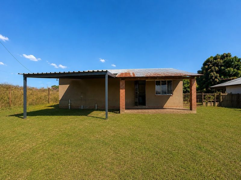 Rear view of a modest house featuring a covered patio area, metal carport structure, and a corrugated metal roof showing signs of weathering.