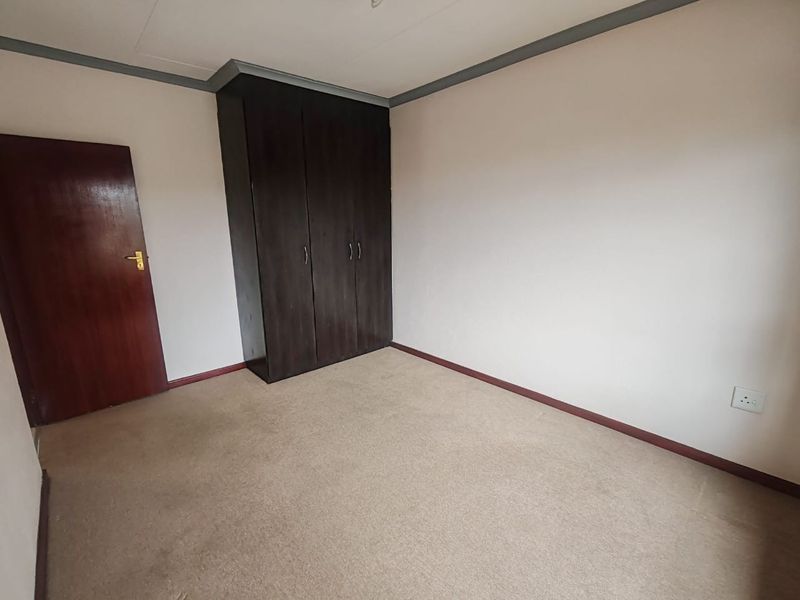 A vacant bedroom featuring neutral walls, carpeted flooring, and a dark wood built-in wardrobe.