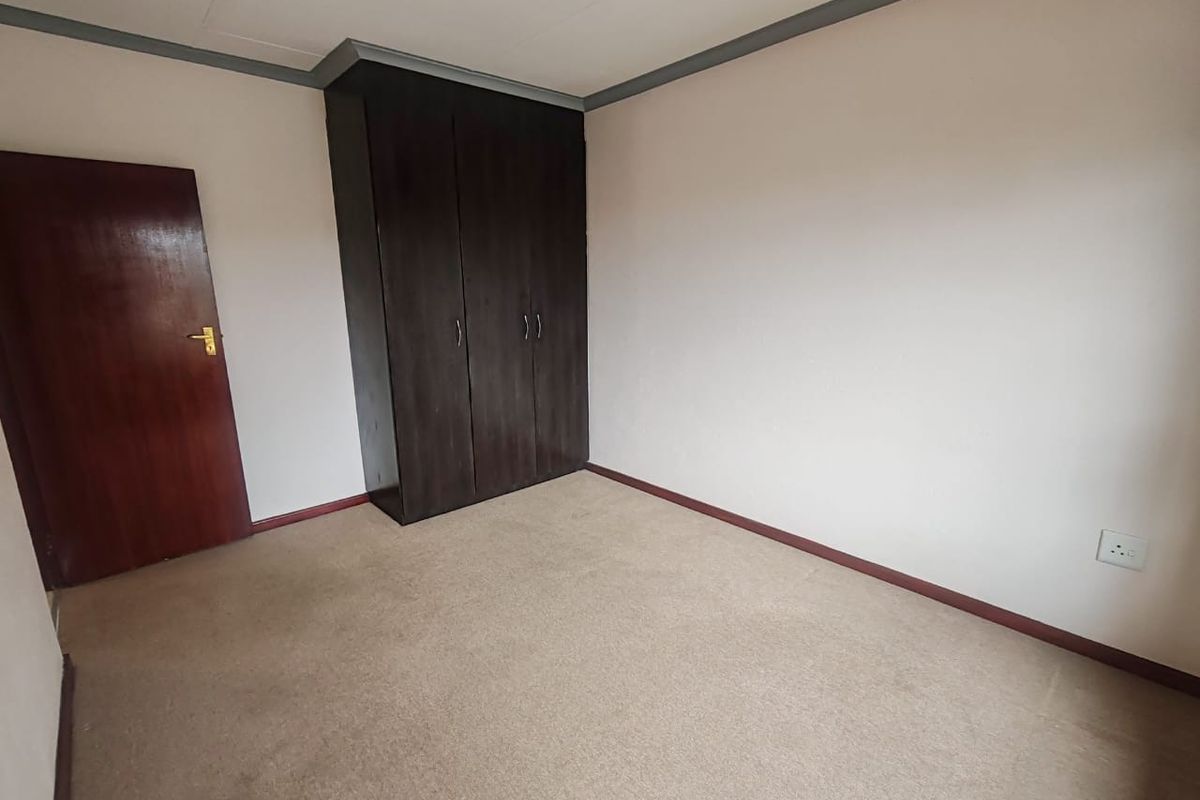 A vacant bedroom featuring neutral walls, carpeted flooring, and a dark wood built-in wardrobe.