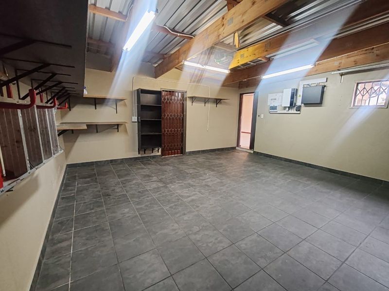 Spacious garage featuring tiled flooring, exposed timber beams, wall-mounted shelving, and an integrated inverter system for power backup.
