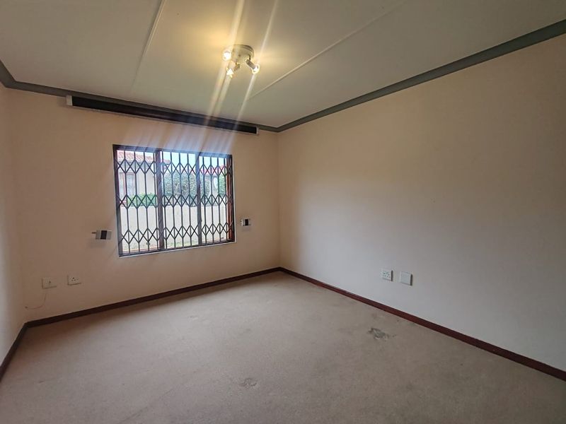 An empty bedroom featuring carpeted flooring, a security gate on the window, and a ceiling light fixture.