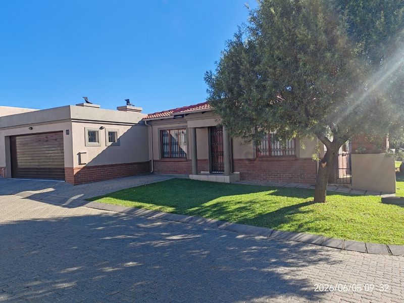 Front view of a townhouse featuring a brick facade, tiled roof, attached garage, and a well-maintained front lawn with a paved driveway.