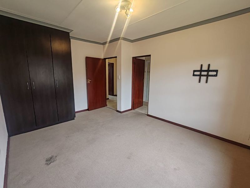 An empty bedroom featuring built-in cupboards, carpeted flooring, and access to an adjoining room.