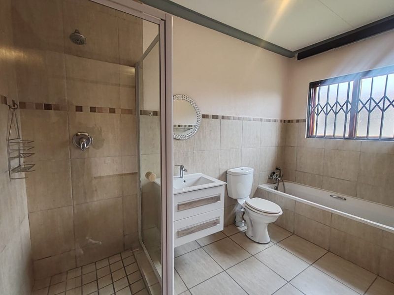 A functional bathroom featuring a separate shower enclosure, bathtub, vanity basin, and toilet, finished with neutral wall and floor tiling.