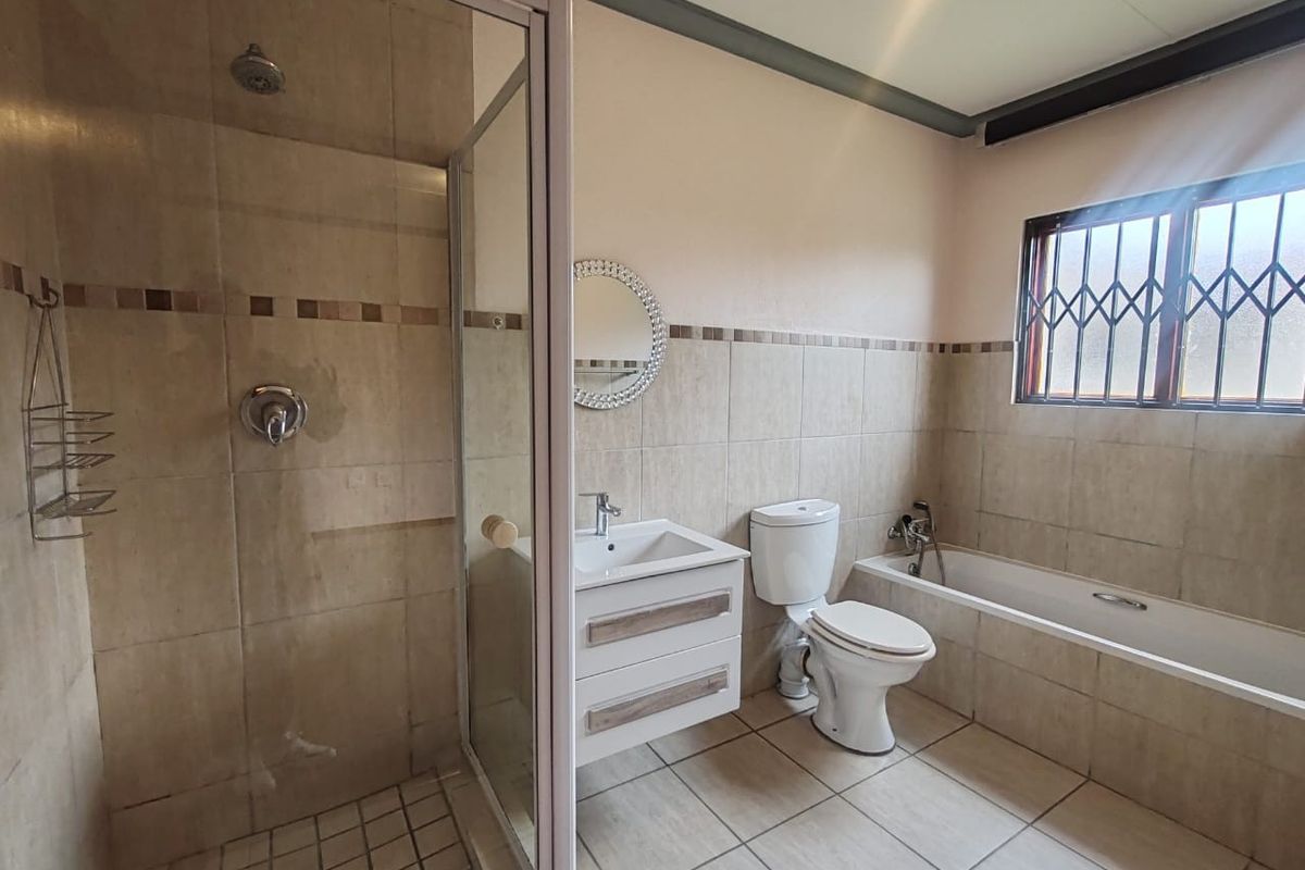 A functional bathroom featuring a separate shower enclosure, bathtub, vanity basin, and toilet, finished with neutral wall and floor tiling.