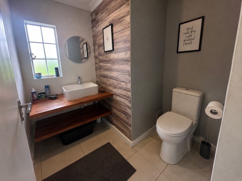A modern bathroom featuring a timber vanity with a vessel sink, a tiled feature wall, and a standard toilet.