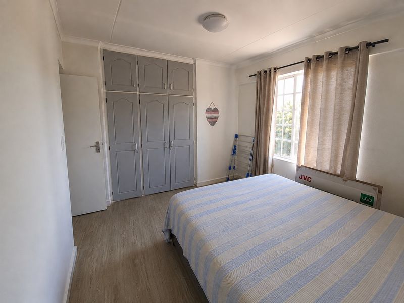 A bedroom featuring laminate flooring and built-in cupboards with overhead storage, providing functional storage space and a neutral aesthetic.