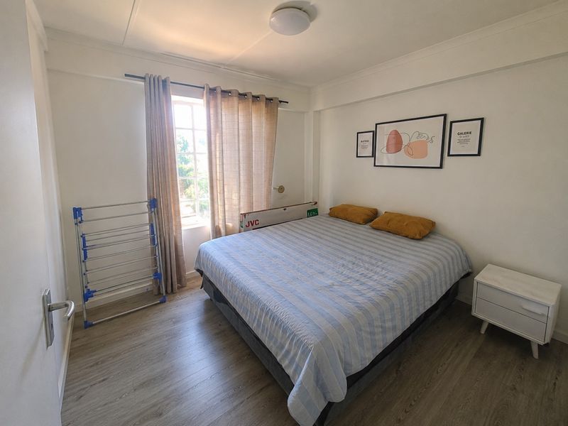 A well-lit bedroom featuring modern laminate flooring and a window with natural light, providing a comfortable and neutral space.
