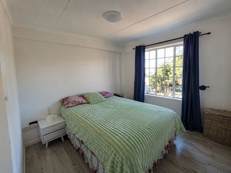 A bright bedroom featuring laminate flooring, a large grid-pane window, and neutral wall finishes, offering a comfortable and functional living space.