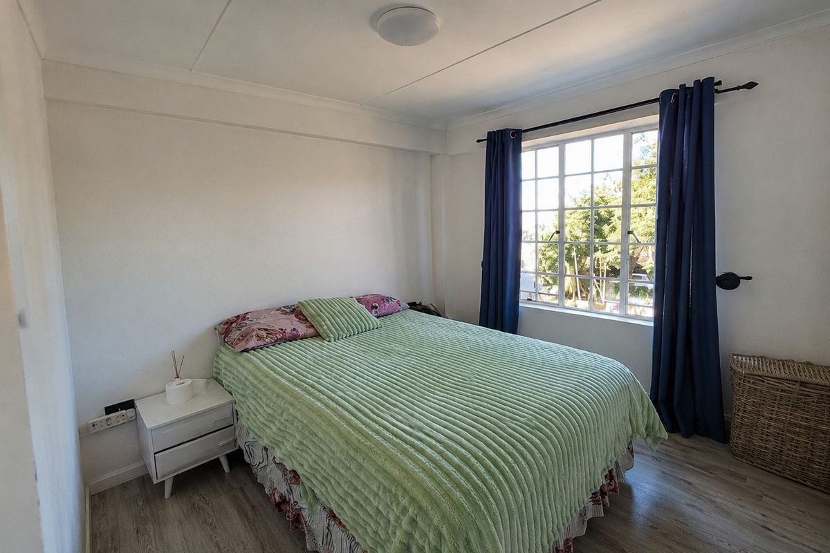 A bright bedroom featuring laminate flooring, a large grid-pane window, and neutral wall finishes, offering a comfortable and functional living space.