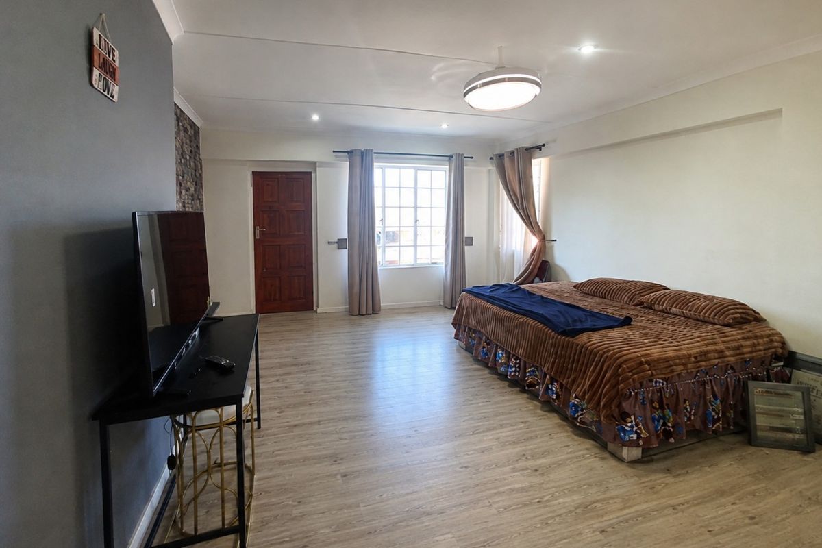 Spacious bedroom featuring laminate flooring, recessed lighting, and a large window with security bars, offering a neutral canvas for personalization.