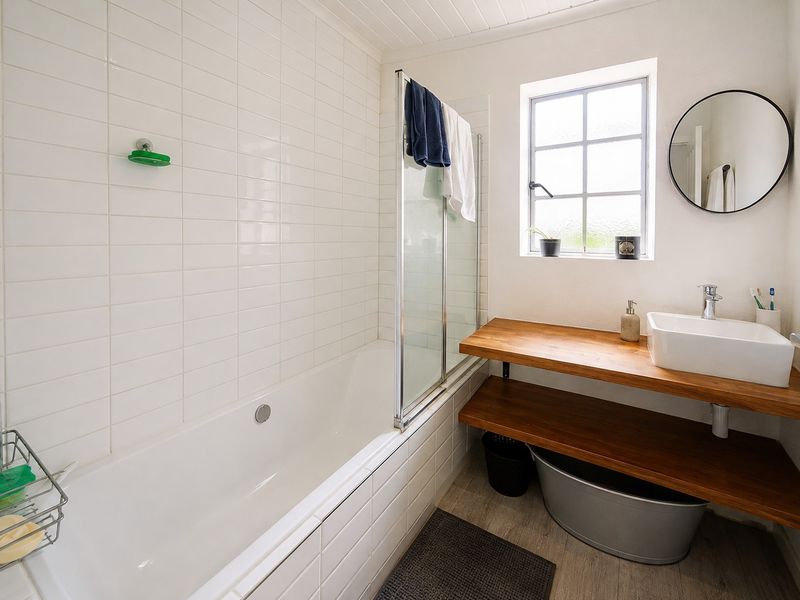 A bright, modern bathroom featuring a white bathtub with a glass screen, a timber vanity shelf with a vessel sink, and tiled walls.