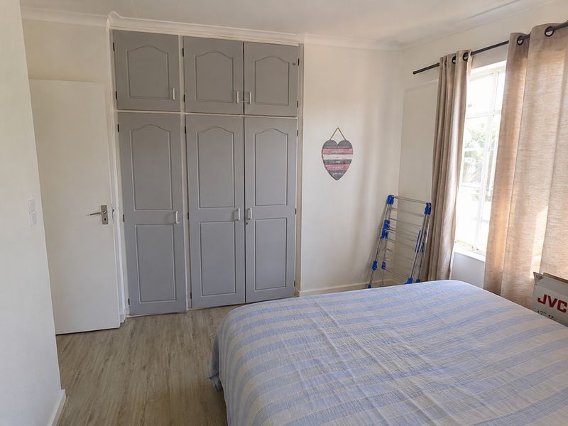 A well-maintained bedroom featuring neutral walls, light laminate flooring, and ample built-in cupboard storage with grey cabinetry.