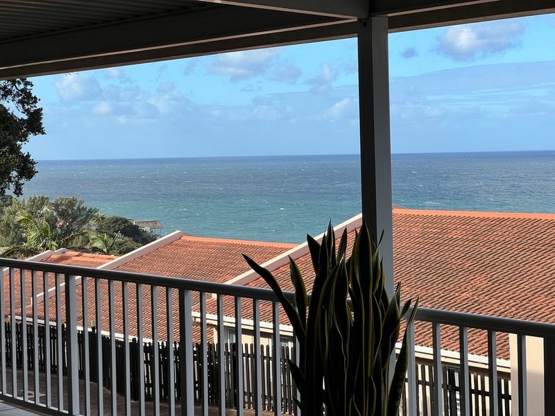 A covered balcony featuring a white railing and offering expansive, elevated ocean views.