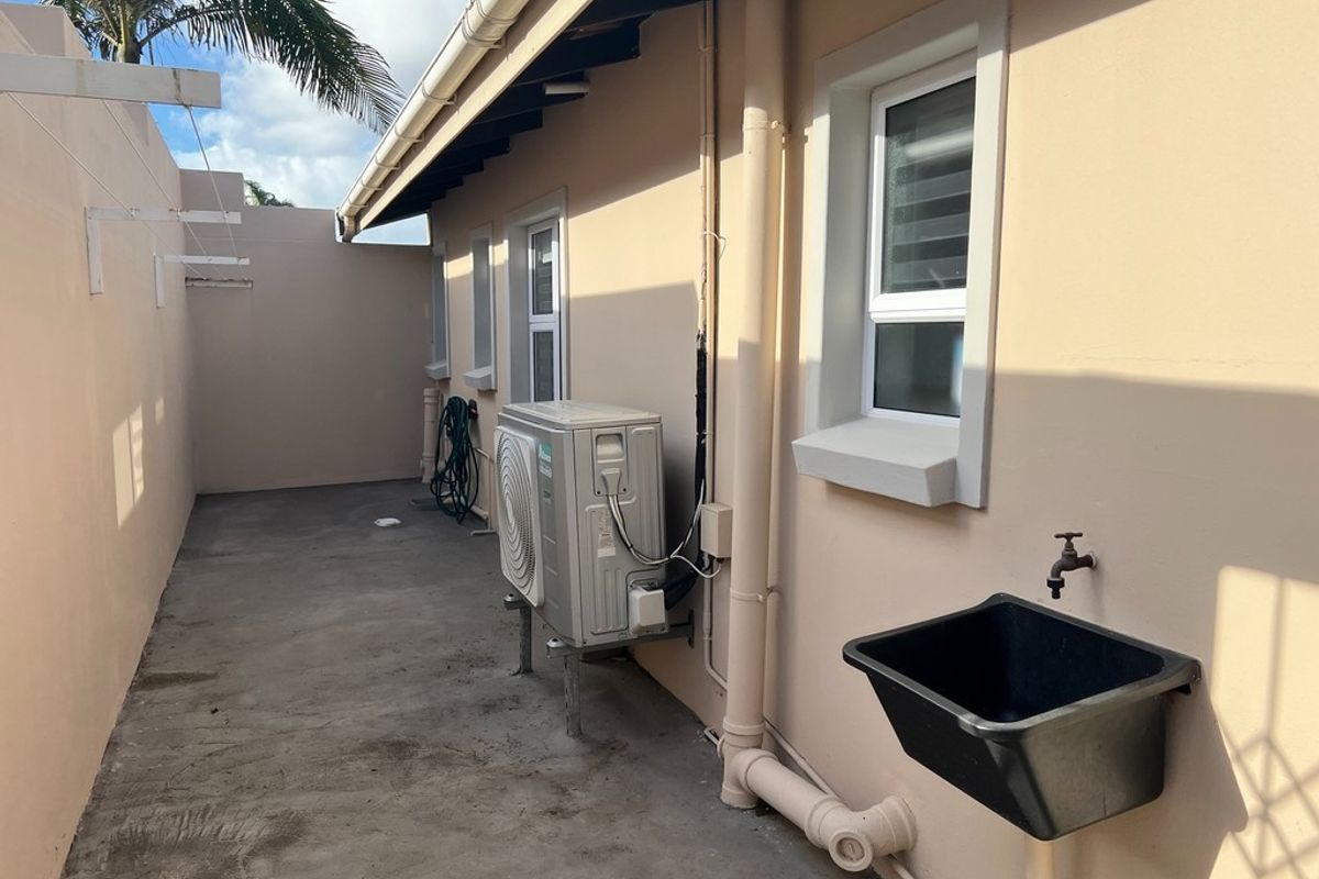 A functional rear exterior utility area featuring a concrete floor, external wash basin, and wall-mounted air conditioning condenser unit.