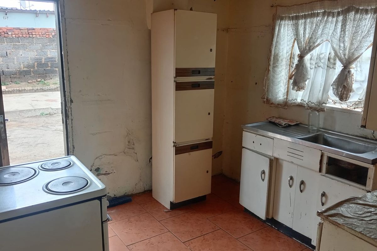 A dated kitchen featuring original cabinetry, a stainless steel sink, and tiled flooring, requiring significant renovation and cosmetic updates to modernize the space.