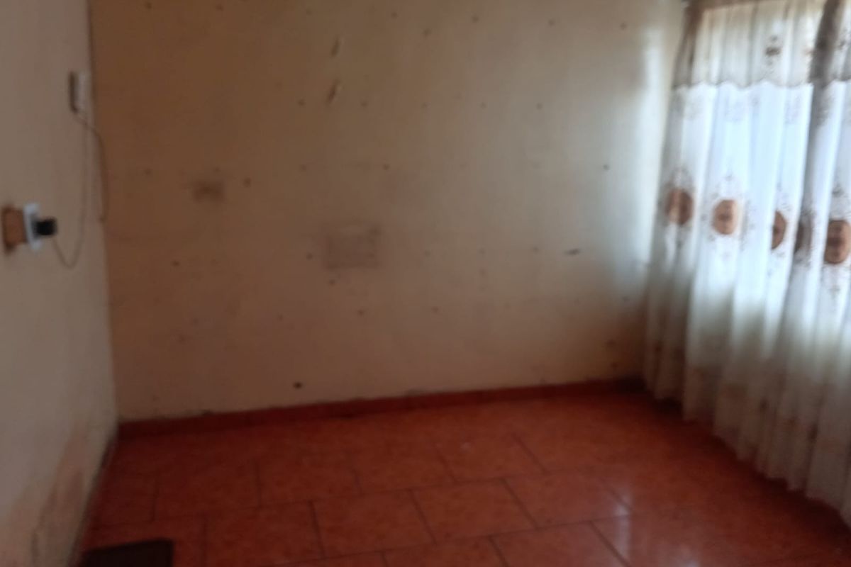 An empty bedroom featuring tiled flooring and wall surfaces in need of repair and repainting.