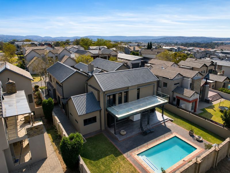 Aerial view of a modern residential property featuring a swimming pool, paved patio, and an upper-level balcony with glass railings.