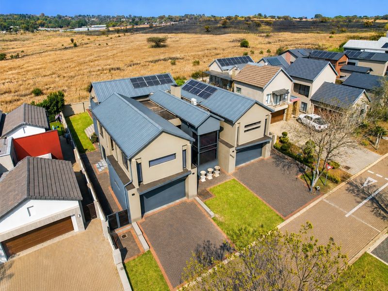 Aerial view of a modern residential property featuring a paved driveway, double garage, and solar panels installed on the metal roof.