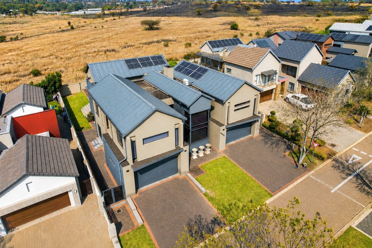 Aerial view of a modern residential property featuring a paved driveway, double garage, and solar panels installed on the metal roof.