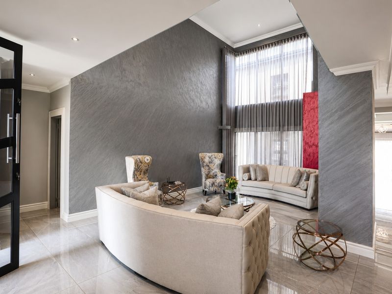 Spacious double-volume living room featuring high ceilings, large floor-to-ceiling windows, elegant textured feature walls, and polished porcelain floor tiles.